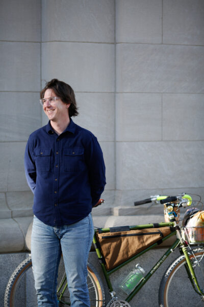 A older white millennial man stands and smiles with his bike. 