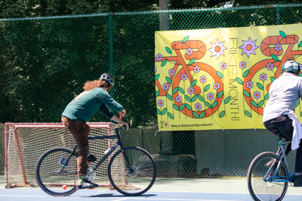 Someone playing bike polo hitting a ball with a mallet into a goal