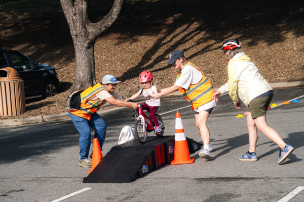 group of 3 adults helping 1 child over a ramp on their bike
