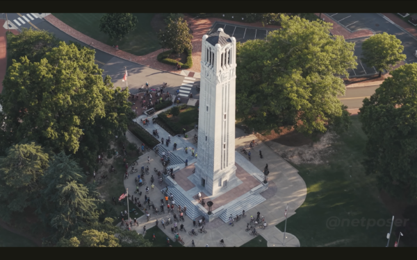 birdseye drone shot of the ncsu bell tower with people standing around it.